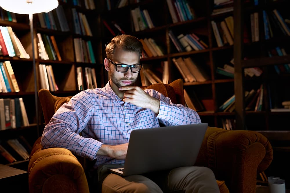 A person studying at a laptop in a library at night.